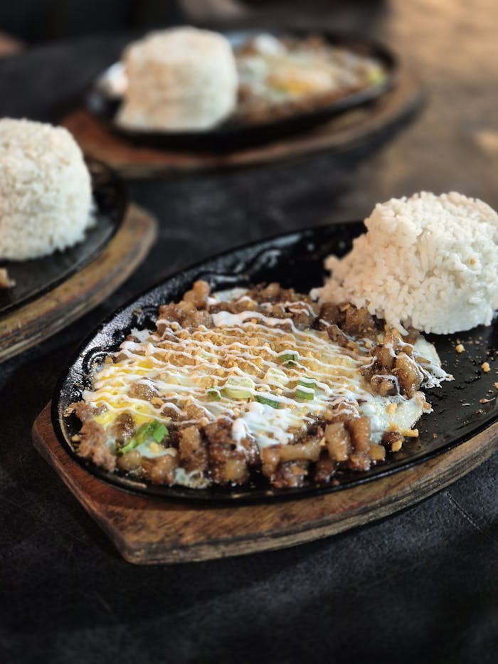 Close-up of sizzling sisig with steamed rice on a hotplate, a popular Filipino dish.