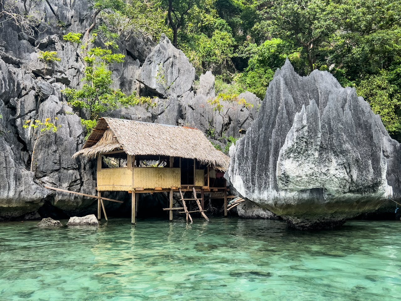 Tranquil bamboo hut by clear waters amidst limestone cliffs in Coron, Philippines.